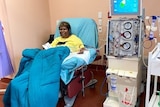 An Aboriginal woman sits at a dialysis chair with a blanket over her. 