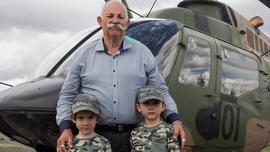 A man and his grandsons stand in front of an army helicopter
