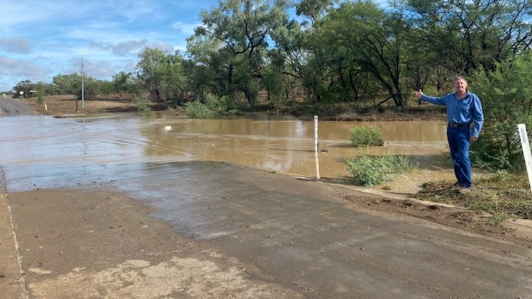 Man stands next to flooded river over road