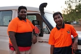 Two Indigenous men in hi-vis shirts standing in front of a Land Cruiser.