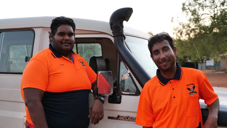 Two Indigenous men in hi-vis shirts standing in front of a Land Cruiser.