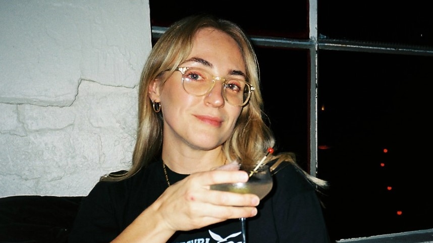 Woman holds a wine glass in darkened club or restaurant and smirks at the camera
