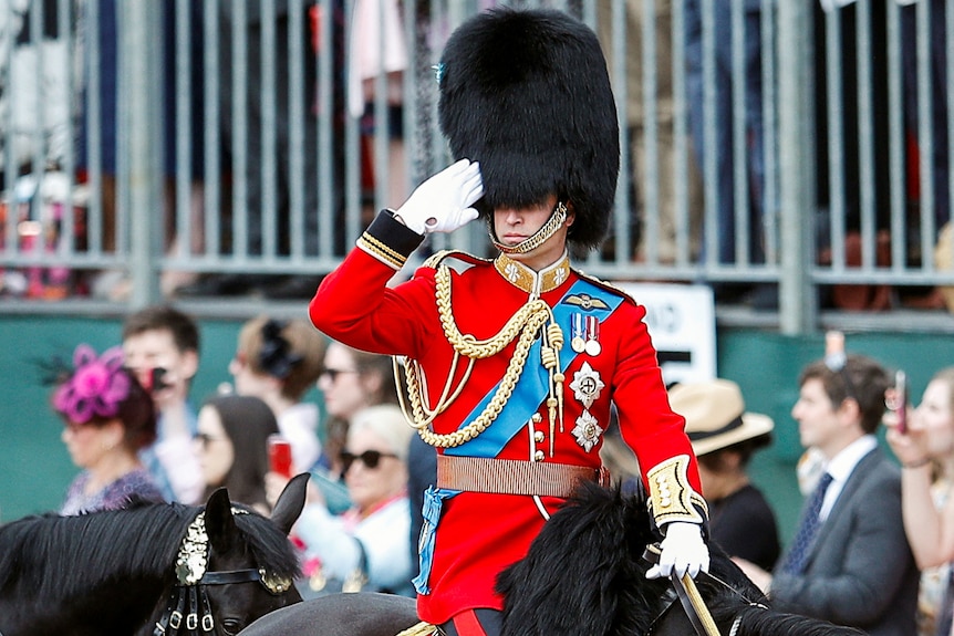 Prince William salutes while riding a horse.