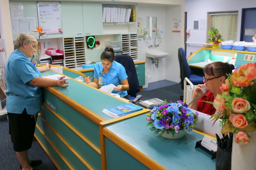 Three nurses work behind a blue counter.