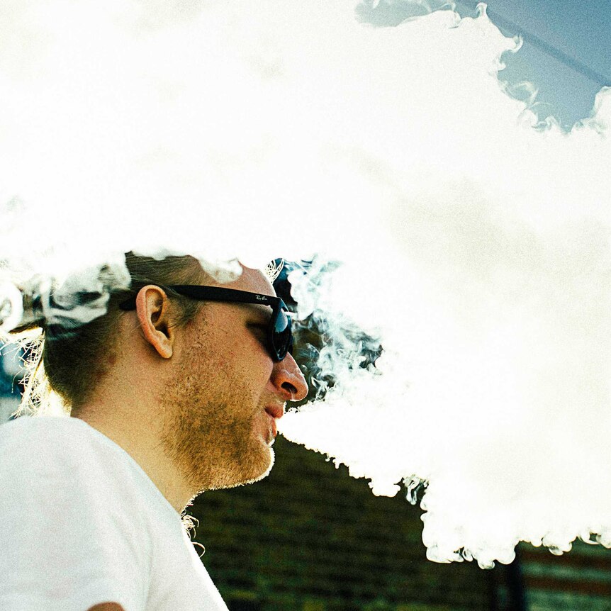 A man vapes surrounded by white smoke.