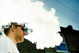A man vapes surrounded by white smoke.