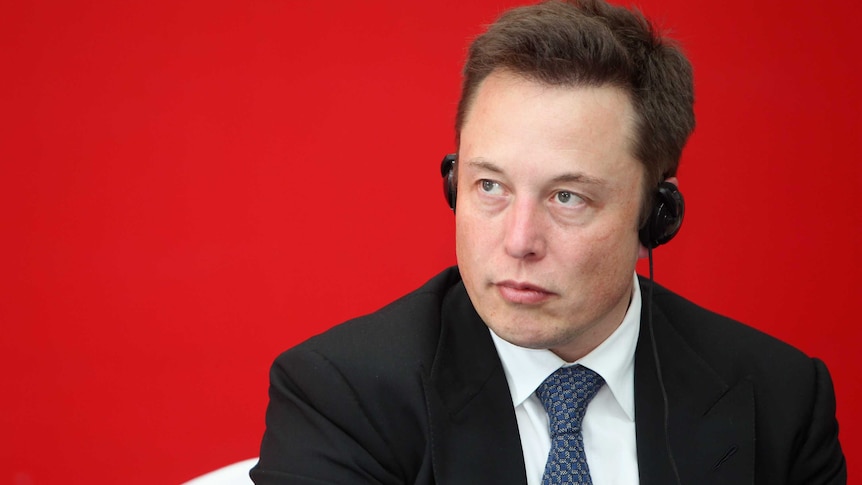 A man sits against a red background with headphones on.