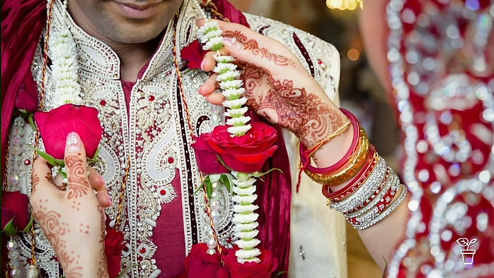 Woman placing a floral garland on a man wearing traditional Hindi dress