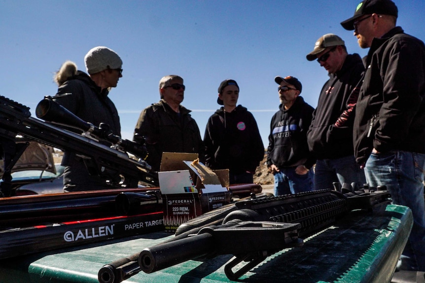 A group of people standing in a semi-circle with a large amount of guns in the foreground