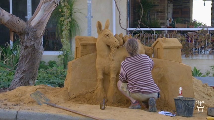 Man working on large goat sand sculpture