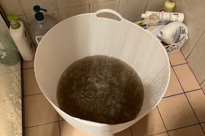 A bucket full of murky water in a shower.