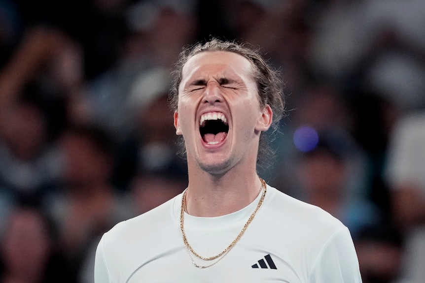Man in a white shirt, eye closed, screaming in celebration on a tennis court.