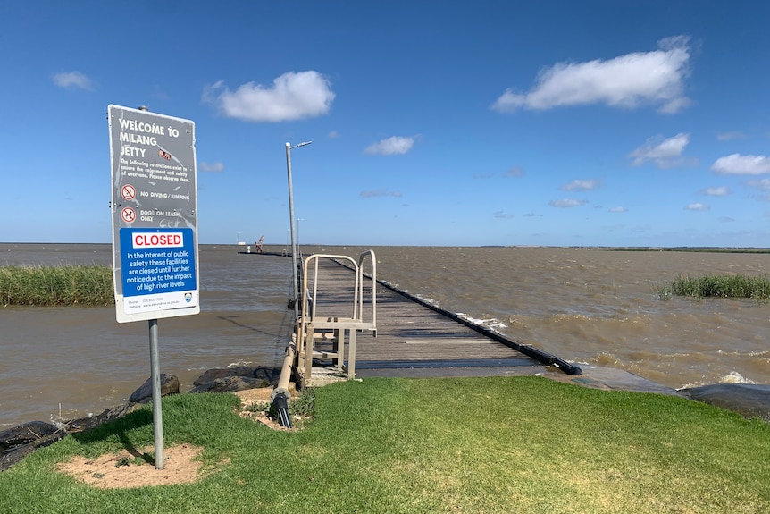 A jetty with water encroaching on it and a CLOSED sign