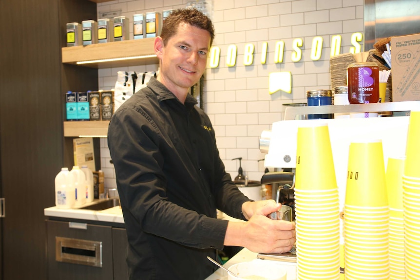 Andrew makes a coffee behind the counter, looking into the camera.