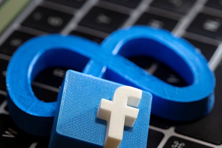 A 3D printed Meta logo and Facebook logo are placed on a laptop keyboard.