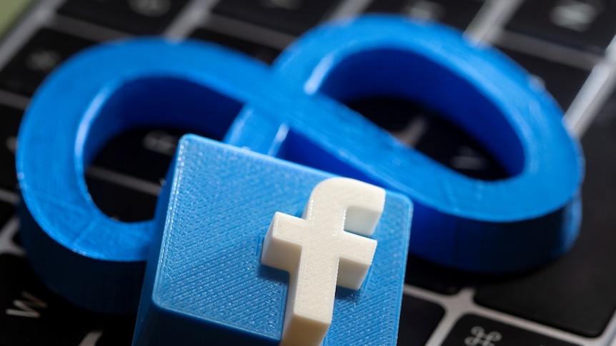 A 3D printed Meta logo and Facebook logo are placed on a laptop keyboard.