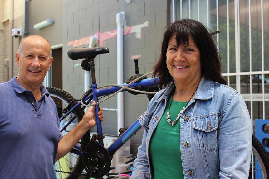 A man and a woman are standing with a broken bicycle.