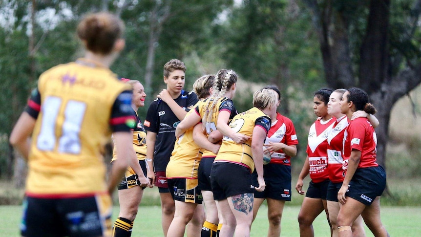 A group of women in yellow and blue footy uniforms face off on the field.