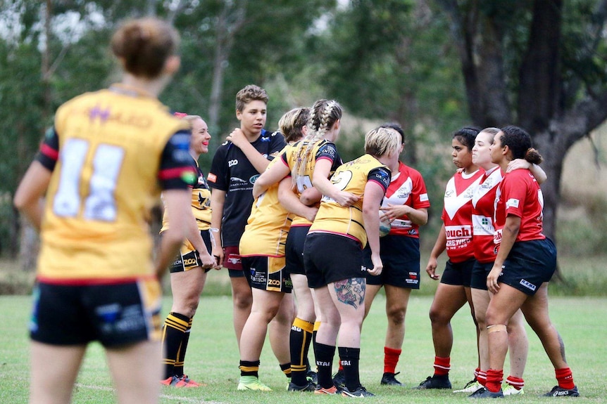 A group of women in yellow and blue footy uniforms face off on the field.