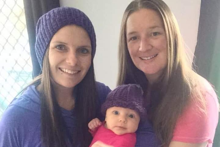 A picture of two women holding a new baby between them.