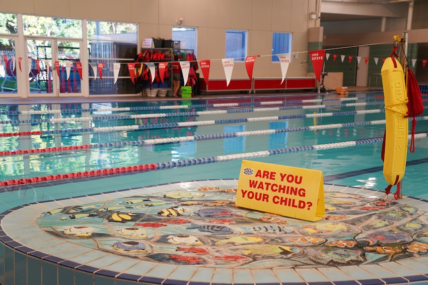 An indoor swimming pool with a small lifesaving sign on a poolside mosaic.