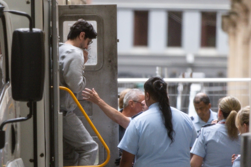 Sako exiting a prison van wearing a gray jumpsuit.