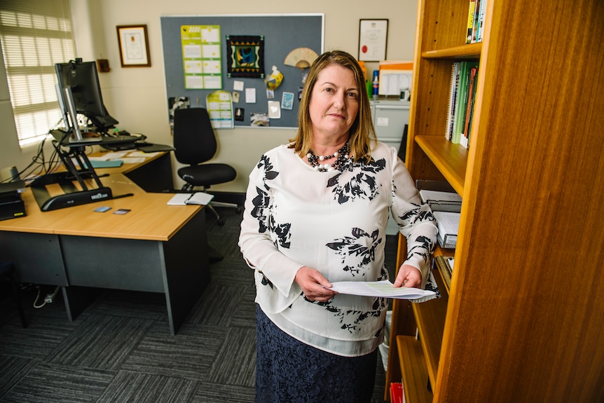 A lady standing in an office holding a piece of paper. 