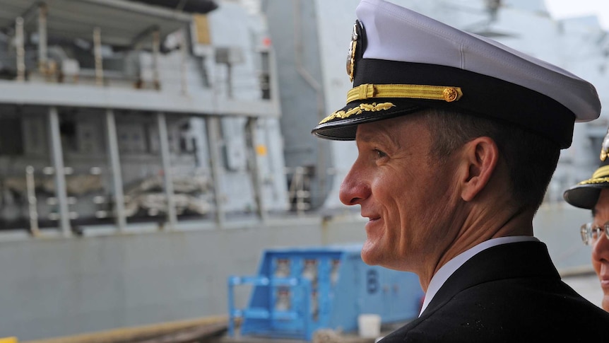 Captain Brett E Crozier looks towards the side of a ship wearing a captains hat.