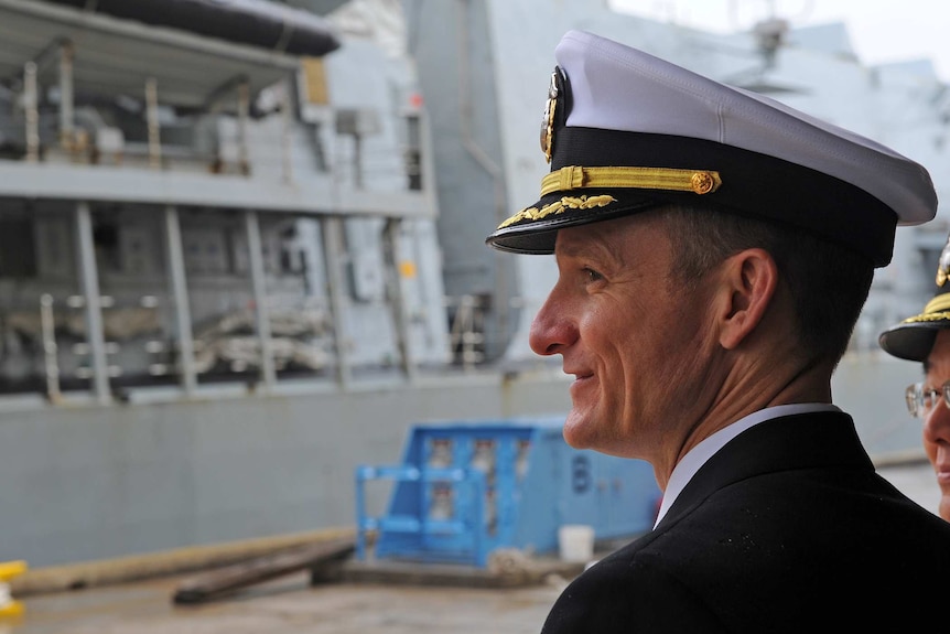 Captain Brett E Crozier looks towards the side of a ship wearing a captains hat.