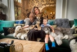 A woman sits on a couch with a small boy and three dogs 