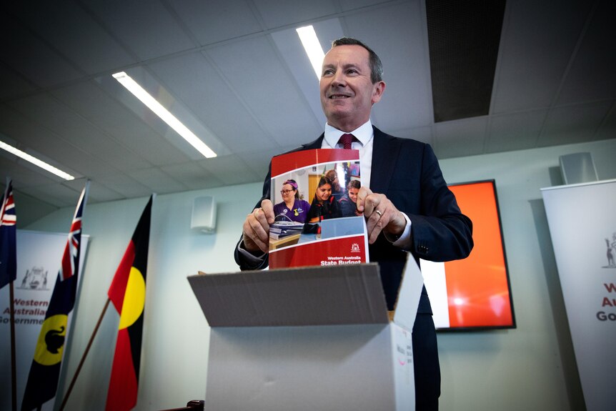 Upshot of WA Premier Mark McGowan at a lectern smiling and holding a budget booklet