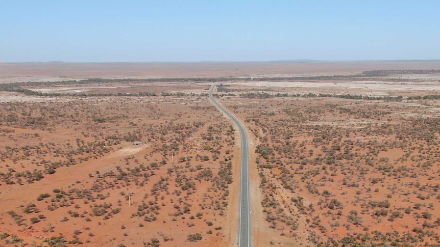 A drone shot of a long stretch of sealed road in the Australian desert.