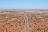A drone shot of a long stretch of sealed road in the Australian desert.