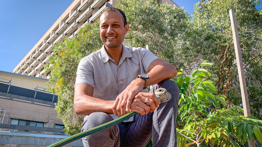 Man holding garden hose on hunkers in front of large tall building.