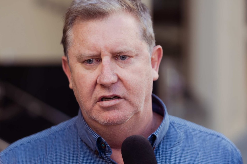 A man in a blue shirt talks into a microphone.