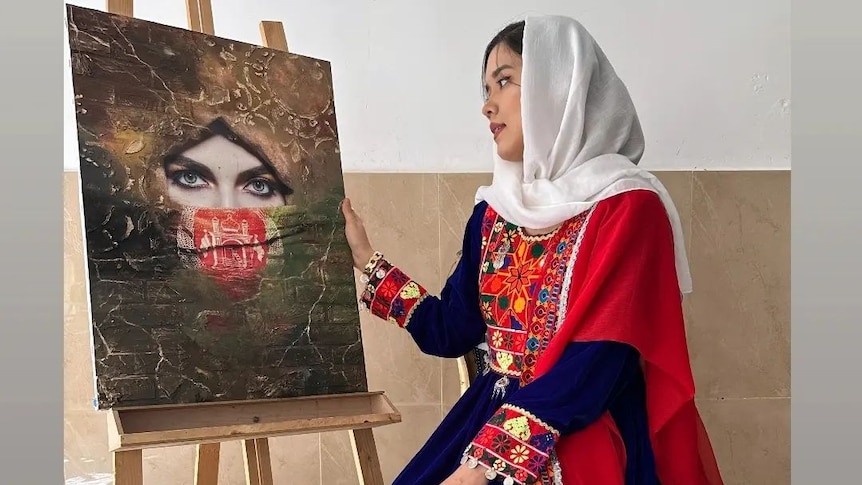 A young woman in a hijab sits in front of an easel bearing a photorealistic artwork.