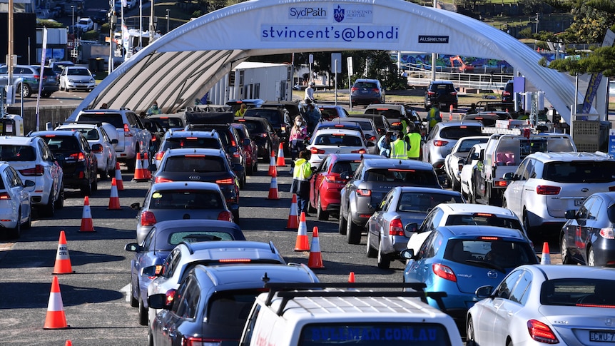 dozens of cars driving into a large testing tent