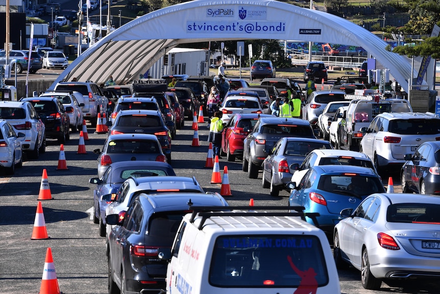 dozens of cars driving into a large testing tent