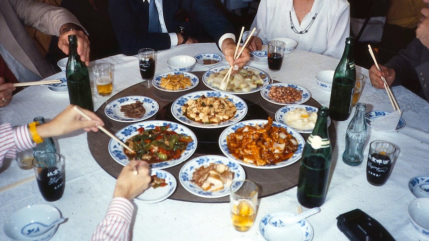 A photo taken with flash shows diners digging into Chinese dishes which are placed on a lazy susan.