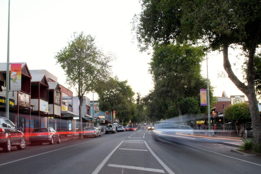 A busy main street with cars parked on the sides and blurred cars moving