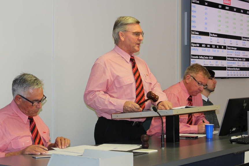 Man wearing pink shirt holding a gavel selling wool.