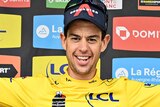 Richie Porte wears a yellow jersey and holds a bunch of flowers and a toy lion in each hand 