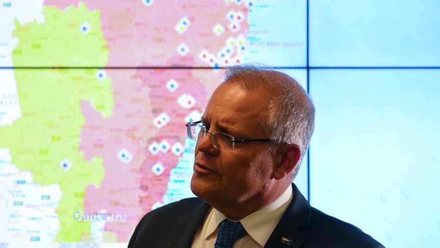The Prime Minister Scott Morrison stands in front of a map that shows fires burning in New South Wales.