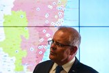 The Prime Minister Scott Morrison stands in front of a map that shows fires burning in New South Wales.