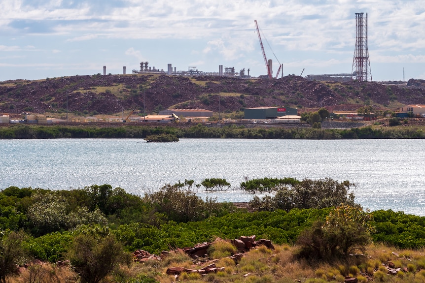 Infrastrutture di pompaggio del gas su larga scala comprese torri e silos situati su una penisola con rocce rosse e oceano blu nelle vicinanze