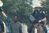 A slightly pixelated image shows two white police officers on horses leading a black man in custody on a leash.