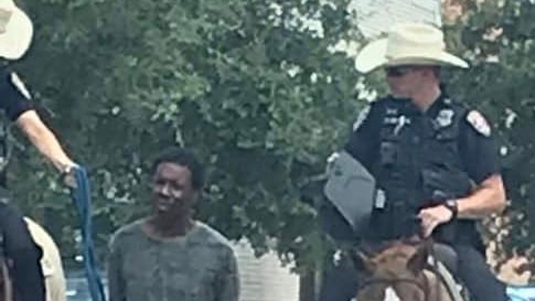 A slightly pixelated image shows two white police officers on horses leading a black man in custody on a leash.