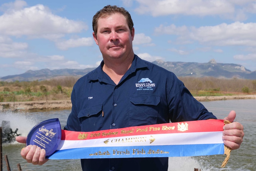 A fish farmer holds a sash and award in front of his fish ponds near Townsville