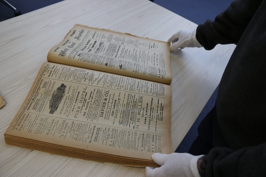 An old news paper is examined by a man with protective white gloves on