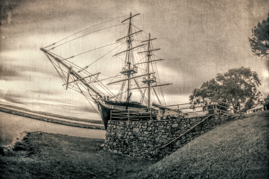 A black and white fish-eye photo of a two-masted tall sailing ship docked in port taken with a pinhole camera